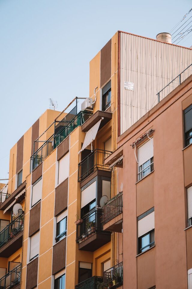 A colourful apartment building with balconies, seen from the street.