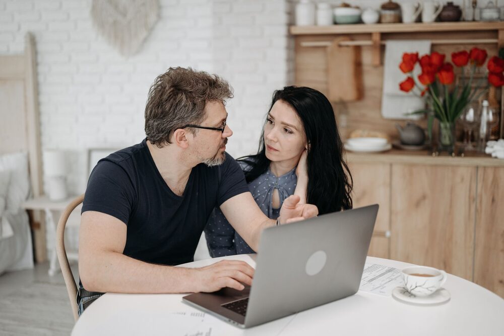 Two people on a couch comparing apartment listings on a laptop.